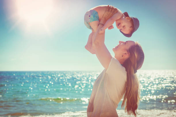 Happy mother and her baby boy playing and having fun on the beach in summer