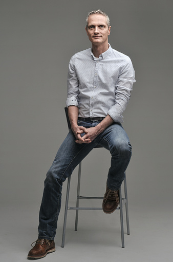 Man in a shirt and jeans is sitting on a chair.