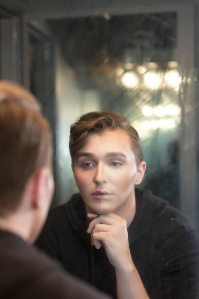 istock Young man in dressing room staring at reflection, wearing make-up 910648442