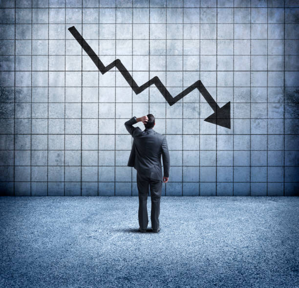 Businessman Looking Up At Downward Trending Arrow With Concern