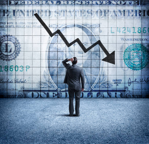 Businessman Looking Up At a Chart That Indicates A Falling U.S. Dollar A rear view of a concerned businessman as he places his hand on his head and looks up at a U.S. One Dollar bill coupled with a downward trending arrow and chart on the wall in front of him. This image illustrates the concept of a falling, or weakening U.S. dollar. deterioration stock pictures, royalty-free photos & images