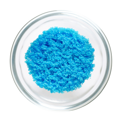 Cupric sulfate in glass bowl, isolated on white background. Bright blue copper sulfate CuSO4, also blue vitriol or bluestone. Salt, used in swimming pools, fireworks and in schools to grow crystals.