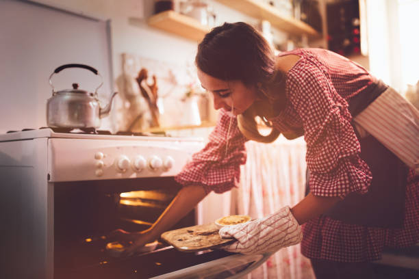 Young woman placing pies in kitchen oven for baking