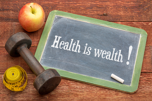 health is wealth concept -  slate blackboard sign against weathered red painted barn wood with a dumbbell, apple and tape measure