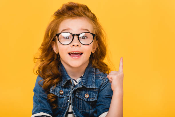 portrait of smiling little kid in eyeglasses pointing up isolated on yellow portrait of smiling little kid in eyeglasses pointing up isolated on yellow alternative pose photos stock pictures, royalty-free photos & images