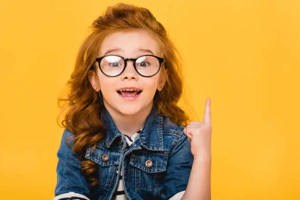 Photo of portrait of smiling little kid in eyeglasses pointing up isolated on yellow