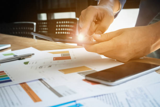 Young business man using tablet with smartphone and graph chart on wood desk for  Plans to improve quality next month in office. Young business man using tablet with smartphone and graph chart on wood desk for  Plans to improve quality next month in office. smart phone telephone research tax stock pictures, royalty-free photos & images