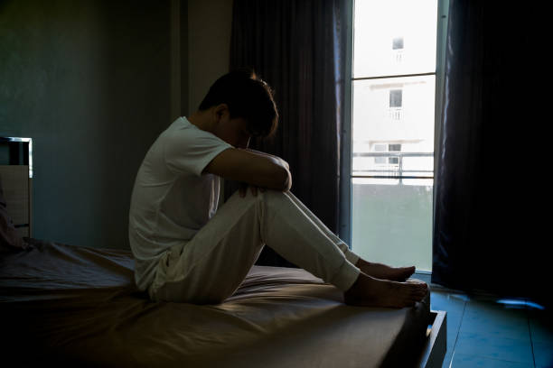 istock Melancholy young man barefoot sitting at the bed embracing his knees, his head down, Feeling problem bored. 910697630