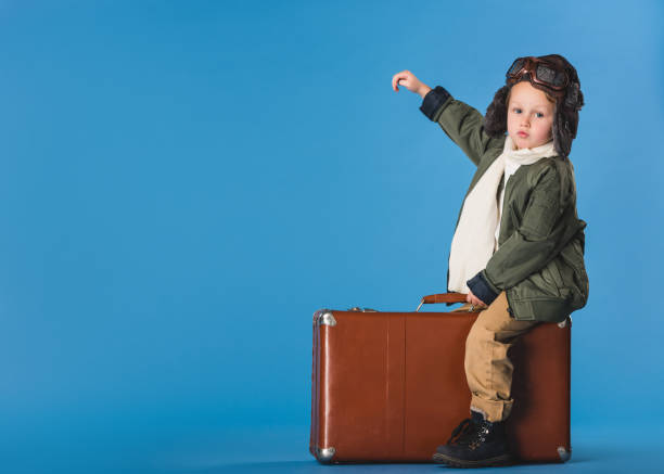 istock side view of boy in pilot costume sitting on suitcase isolated on blue 910697928