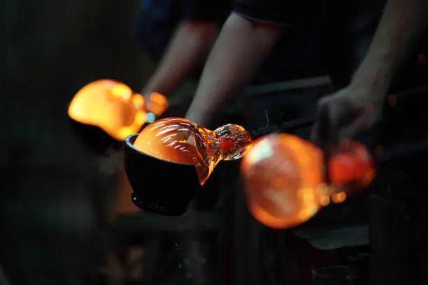 Process of shaping glass during handmade production. Workers use special equipment to create glass ball.