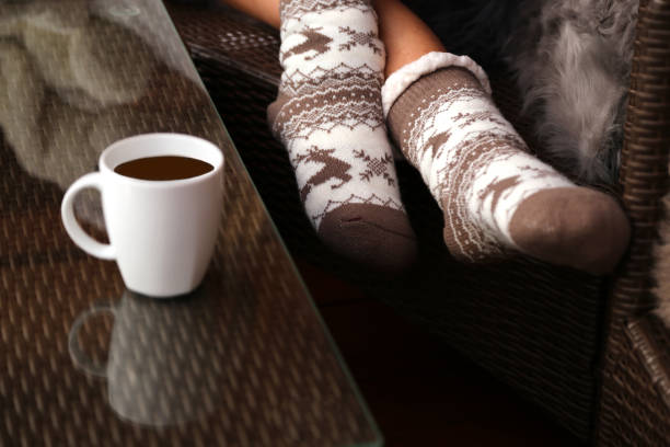girl legs in stylish warm sock in garland lights on floor with rug in festive room. decor for winter holidays. atmospheric moment. cozy winter days