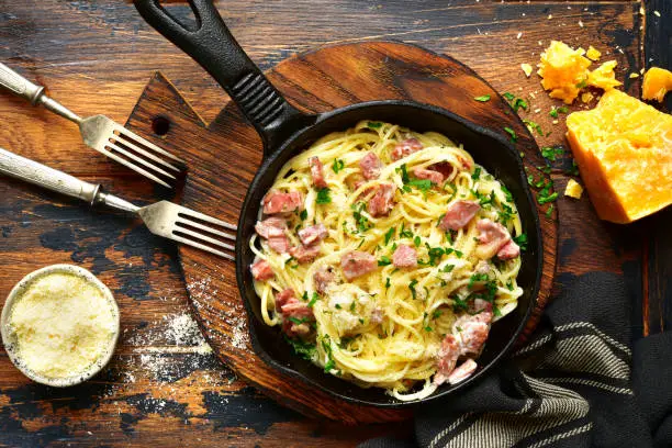 Traditional italian dish spaghetti carbonara with bacon in a cream sauce in a skillet over dark wooden background.Top view with copy space.