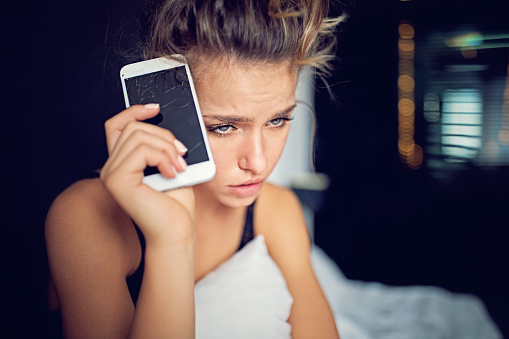 Depressed young woman with broken smartphone.