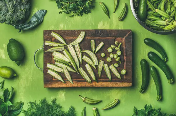 Healthy vegan cooking ingredients. Flay-lay of green vegetables and greens on wooden board over green background, top view. Clean eating, vegetarian, detox, dieting food concept
