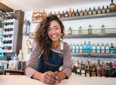 Portrait of friendly waitress working at a restaurant and leaning on the bar while looking at the camera smiling