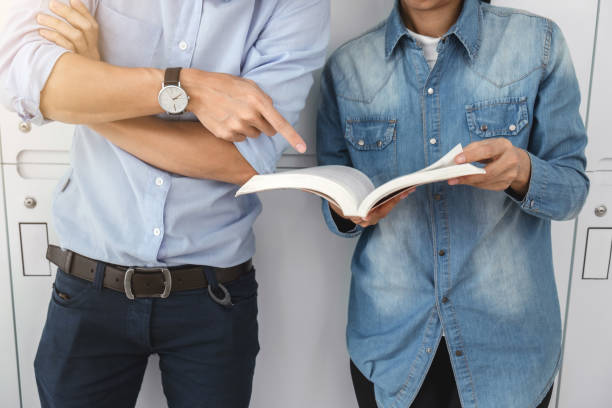 istock Cheerful young student standing holding book and reading, classmates helps friend catching up workbook and learning tutoring lean on locker, teaching, learning, People, Education and school concept 910725588