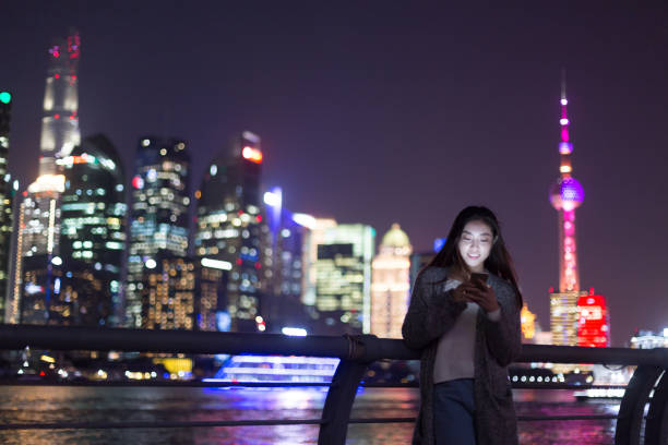 junge asiatische frau spielt mit handy in modernen stadt - shanghai skyline night urban scene stock-fotos und bilder