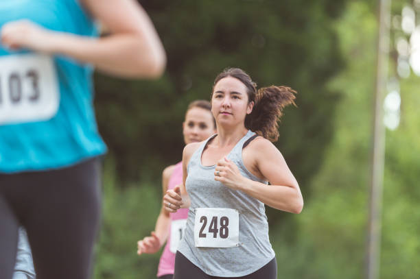 Fundraising Run Group of women run to raise money for breast cancer research. They are wearing race bibs and are on a sidewalk, with trees on the left side. walking for a cause stock pictures, royalty-free photos & images