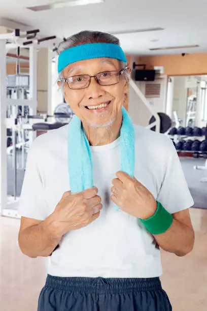 Portrait of elderly man smiling at the camera while standing in the fitness center
