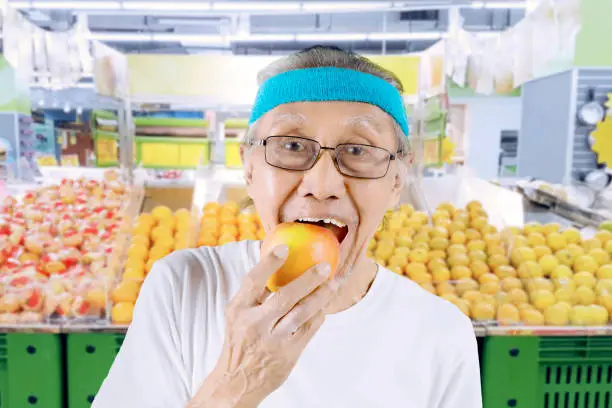 Closeup of elderly man eating a fresh apple while standing in the supermarket