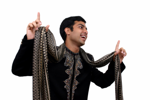 Waist-up view of laughing Middle Eastern man in traditional attire standing under mudbrick archway and looking at camera.