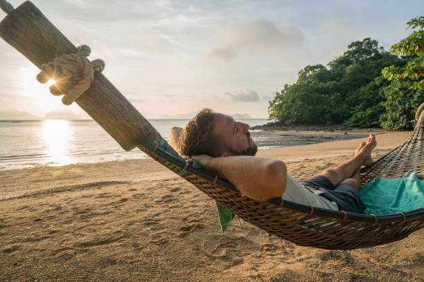 istock Young man enjoying sunset from beach hammock 910779462