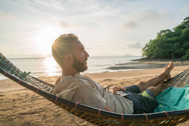 istock Young man enjoying sunset from beach hammock 910779482