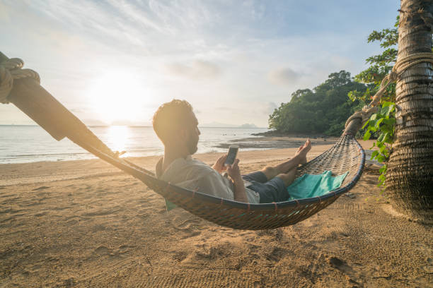 man on hammock using mobile phone, thailand - hammock beach vacations tropical climate imagens e fotografias de stock