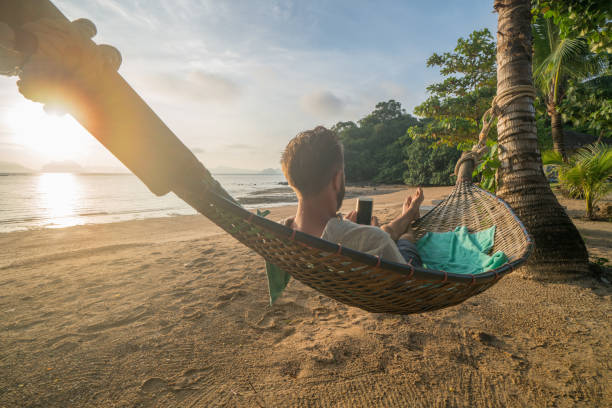 istock Man on hammock text messaging on mobile phone, Thailand 910779608