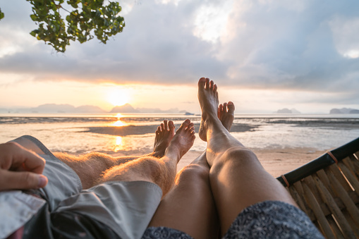Couple's point of view from hammock on the beach at sunrise, barefoot.