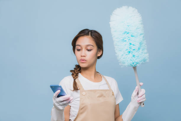 mujer joven mirando teléfono inteligente mientras que limpiar la casa durante la limpieza. - clean e mail cleaning clipping path fotografías e imágenes de stock