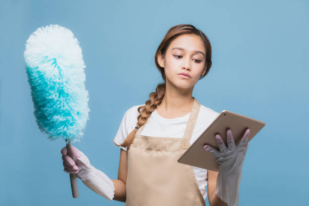 mujer joven mirando teléfono inteligente mientras que limpiar la casa durante la limpieza. - clean e mail cleaning clipping path fotografías e imágenes de stock