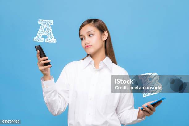 Young Woman Comparing Smartphone A With Smartphone B Stock Photo - Download Image Now
