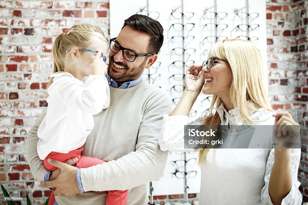 Family in Optics Store Four year little girl in optics store choosing glasses with her father. Ophtamologist helping. Eyeglasses Stock Photo