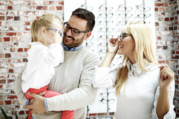 Family in Optics Store Four year little girl in optics store choosing glasses with her father. Ophtamologist helping. group of people wearing eyeglasses stock pictures, royalty-free photos & images