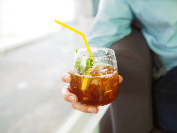 Holds a glass of ice black tea with ginger ale decorated with lemon sliced and mint. Holds a glass of ice black tea with ginger ale decorated with lemon sliced and mint. Lifestyle concept. quench your thirst pictures stock pictures, royalty-free photos & images