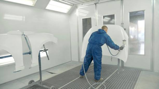 istock Auto painter spraying white paint on car hood in special booth 910797762