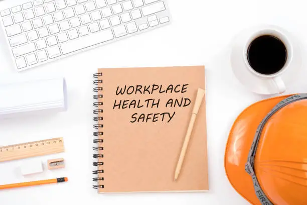 Workplace health and safety concept. Top viwe of modern workplace with safety helmet, office supplies, a cup of coffee and keyboard on white background.