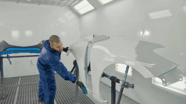 istock Auto painter spraying white paint on car spare fender in special booth 910801870