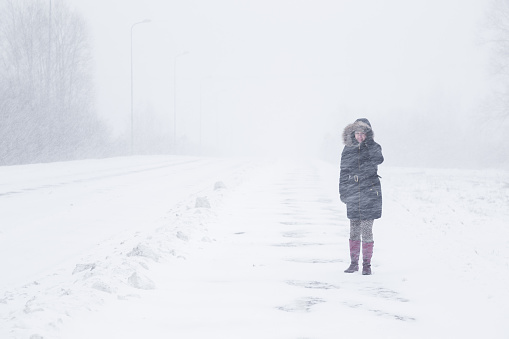 Winter is coming by snow. Poor visibility in heavy snow storm on path. Woman slowly and hard walking in dangerous weather day. Cataclysm of nature. City people life in blizzard concept.