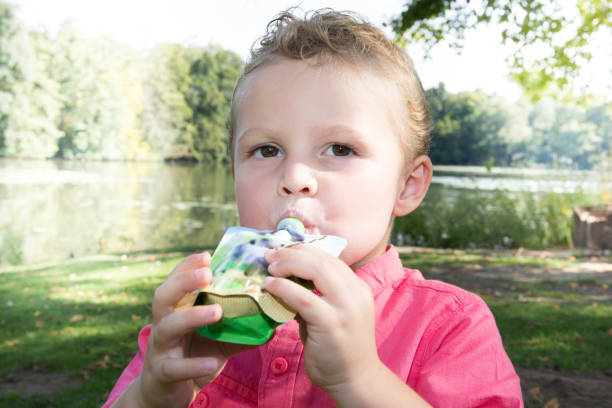 child sitting in the grass eating applesauce in a gourd young boy eat in park a fruit compote in a gourd compote stock pictures, royalty-free photos & images