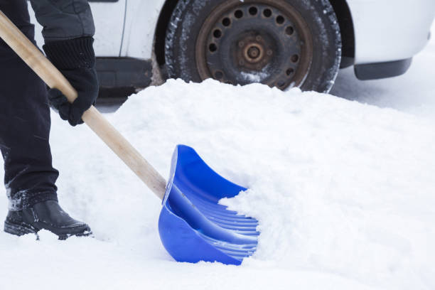 istock Man with blue shovel removing snow front of car wheel in winter day. Winter routine and problem concept. 910829794