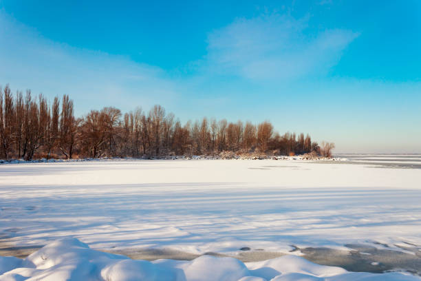 istock a frozen river by the shore of a forest under a blue sky 910832538