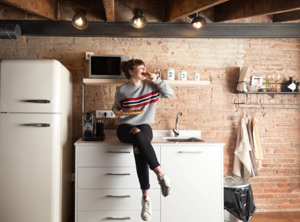 beautiful girl eating pizza in a modern kitchen - modern handmade imagens e fotografias de stock