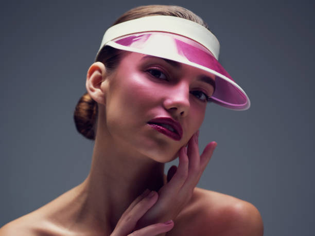 Studio shot of an attractive young woman wearing a pink retro cap posing against a gray background