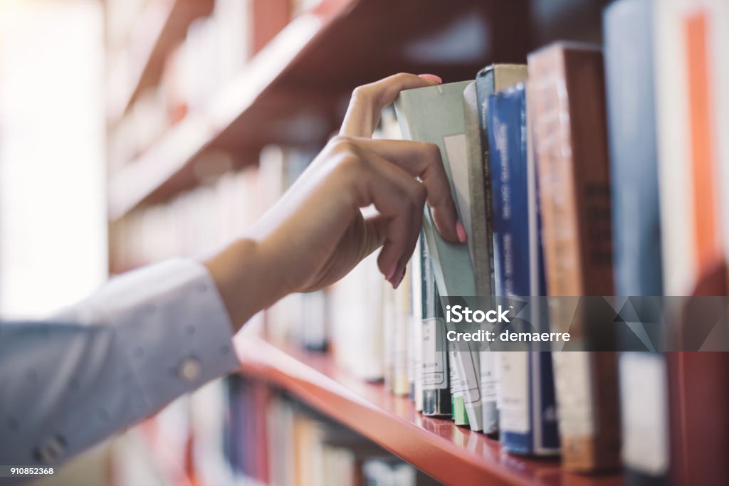 Student searching books Woman at the library, she is searching books on the bookshelf and picking a textbook, hand close up Library Stock Photo
