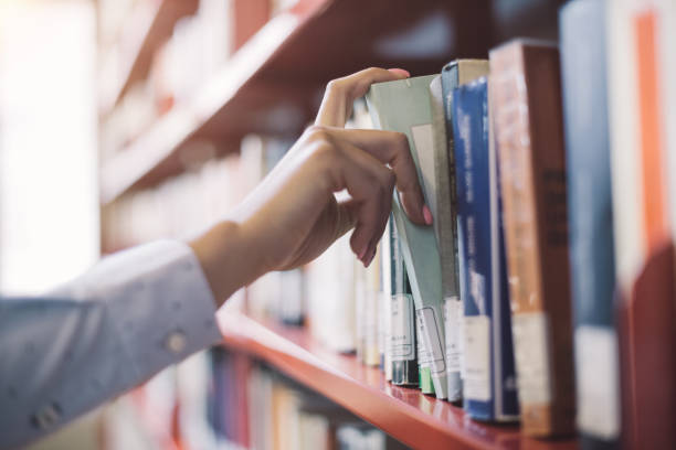 Student searching books Woman at the library, she is searching books on the bookshelf and picking a textbook, hand close up book display stock pictures, royalty-free photos & images