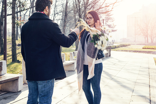 Irritated young woman pushing aside bouquet of flowers from her boyfriend