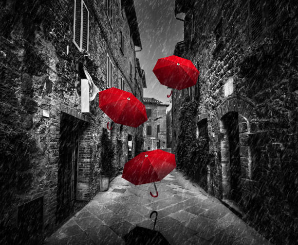 umrbellas volando con viento y lluvia en una calle oscura en un pueblo del viejo italiano en toscana, italia - lluvia fotos fotografías e imágenes de stock