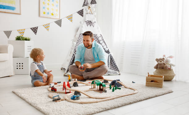 glückliche familie, vater und kind sohn in spielzeug-eisenbahn im spielzimmer spielen - child playroom parent indoors stock-fotos und bilder